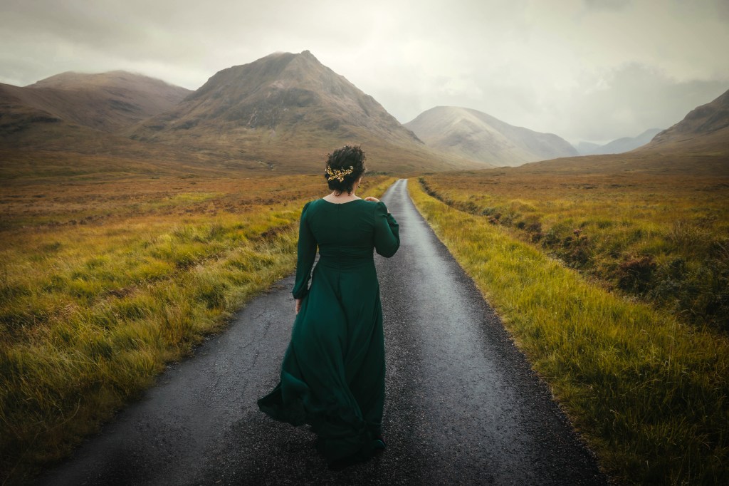 Cari Powell of Selkie Sisters Travel walking a single-track road through a Highland glen